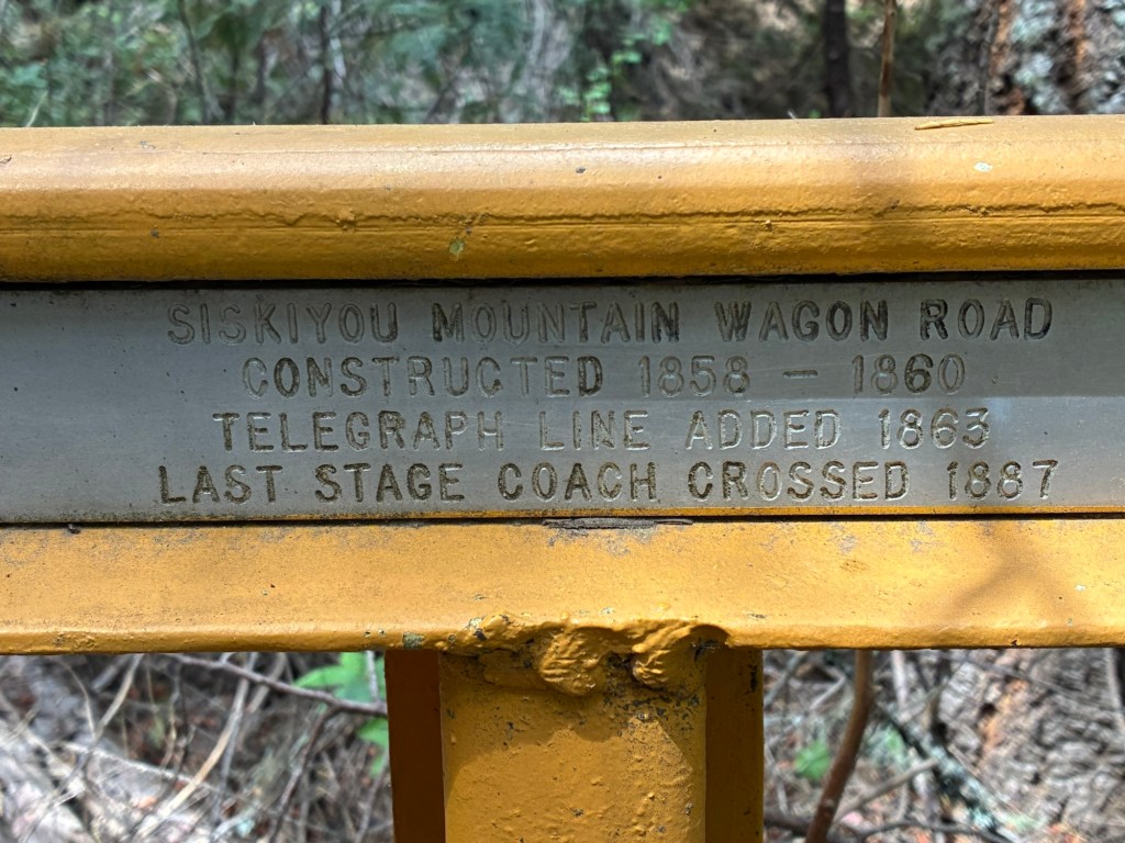 Historical marker reading "Siskiyou Mountain Wagon Road. Constructed 1858-1860, telegraph line added 1865, last stage coach crossed 1887."