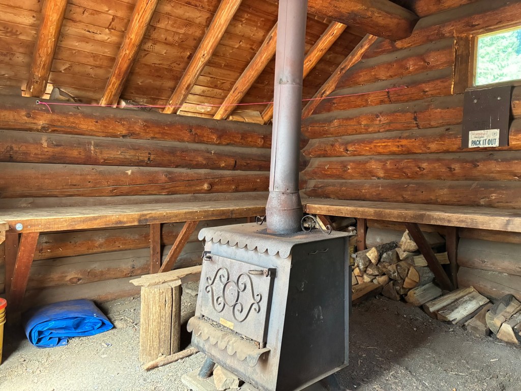 Interior view of the shelter showing a woodstove in the center and bunks along the walls